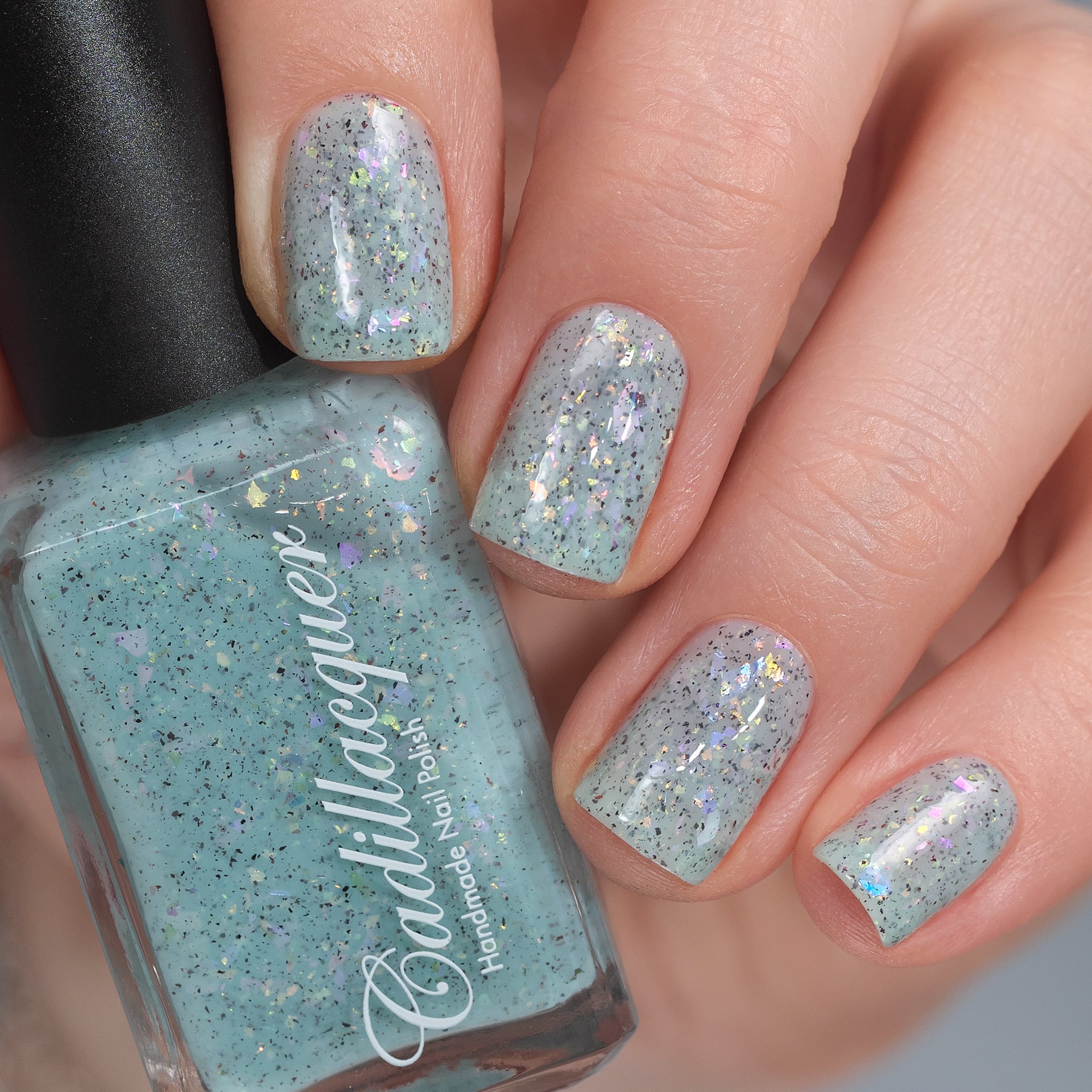 Cadillacquer Fresh Sheets pastel mint iridescent crelly nail polish, bottle held with four-nail swatch, light skin, studio lighting