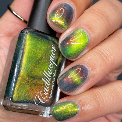 Magnetic multichrome Cadillacquer nail polish in I Found A Place, showing the bottle held in hand alongside four swatched squoval nails, the polish shifts from deep dark teal in the field regions through electric lime-chartreuse along the magnetic band stripe, with red-to-copper aurora shimmer throughout, light skin tone, studio lighting, swatched by @heeymercedes