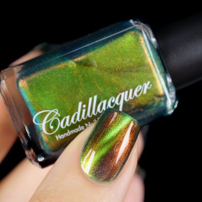 Magnetic multichrome shimmer Cadillacquer nail polish in I Found A Place, shown in bottle held in hand with one swatched nail visible, shifting from deep teal base through lime green magnetic band to copper-bronze at low angles with red-orange aurora shimmer particles throughout, light-medium skin tone, bright daylight lighting, swatched by @yyulia_m