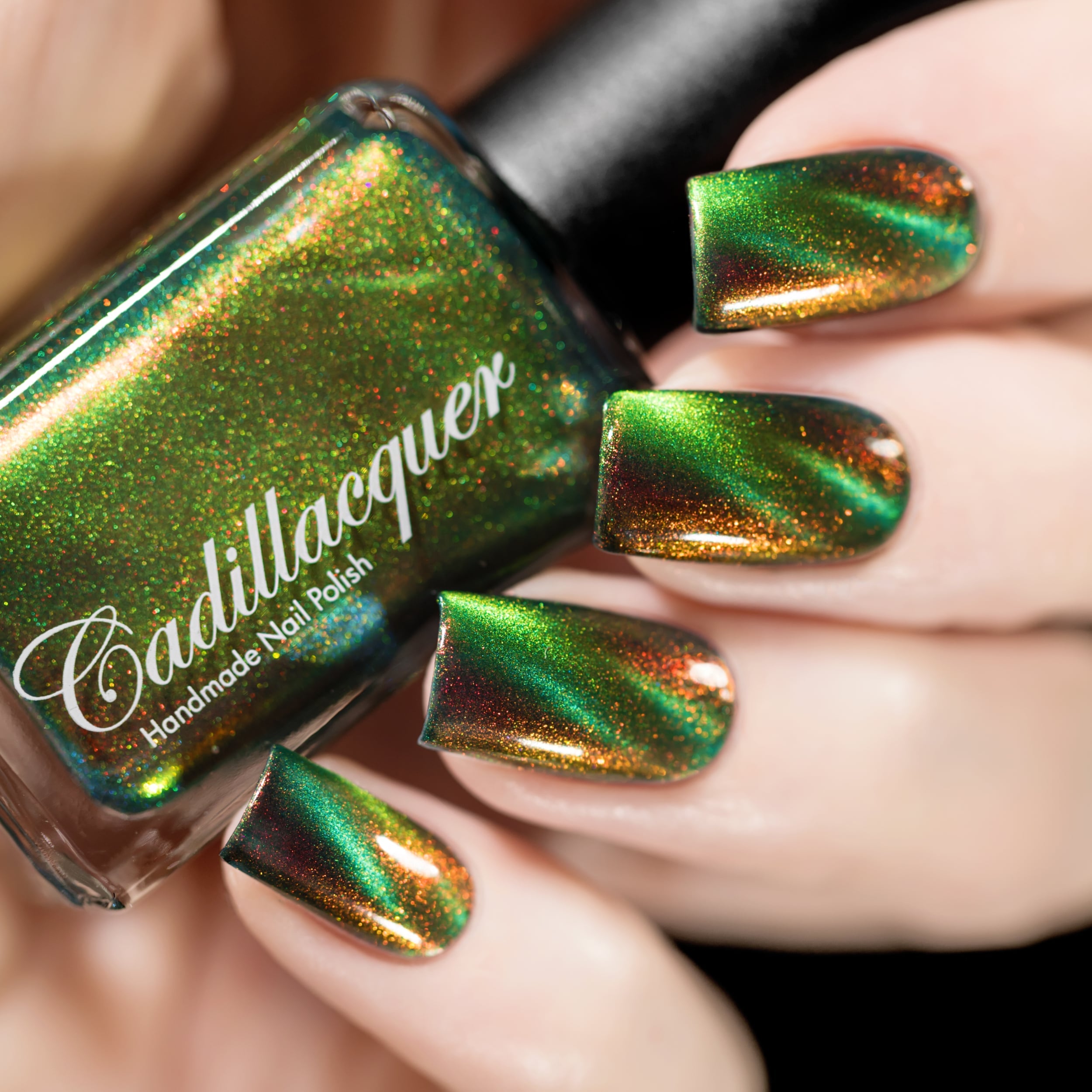 Magnetic multichrome shimmer Cadillacquer nail polish in I Found A Place, shown in bottle held in hand alongside four square nails swatched in deep forest green shifting through lime green magnetic band, amber-orange and deep red aurora shimmer, light skin tone, studio lighting, swatched by @rafinails