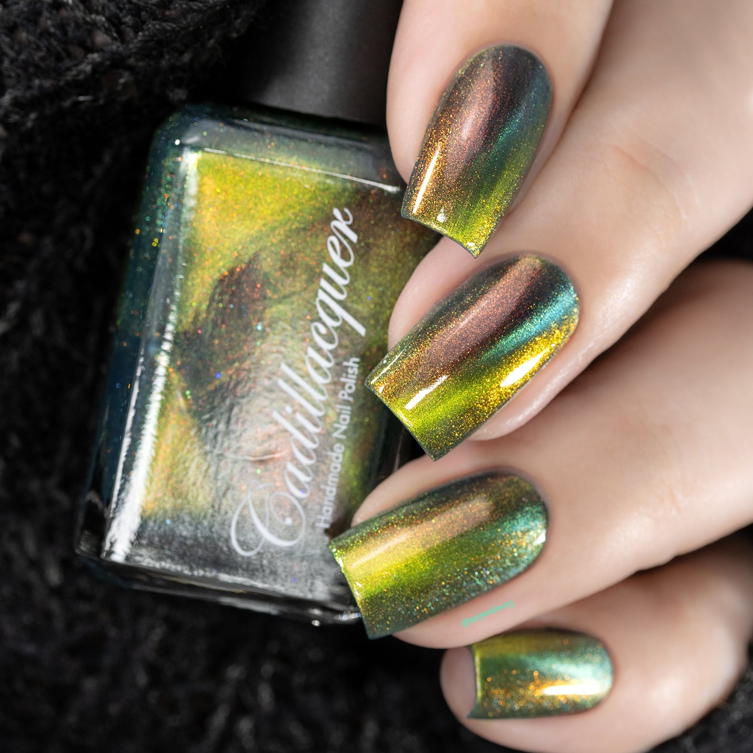 Magnetic multichrome holographic Cadillacquer nail polish in I Found A Place, shown as a hand swatch on five square nails with a bottle alongside, nails shift from deep teal field through olive-lime and chartreuse-gold magnetic band to burnt copper-red aurora flash, with fine holographic shimmer throughout, light-medium skin tone, studio lighting, swatched by @serpentine13