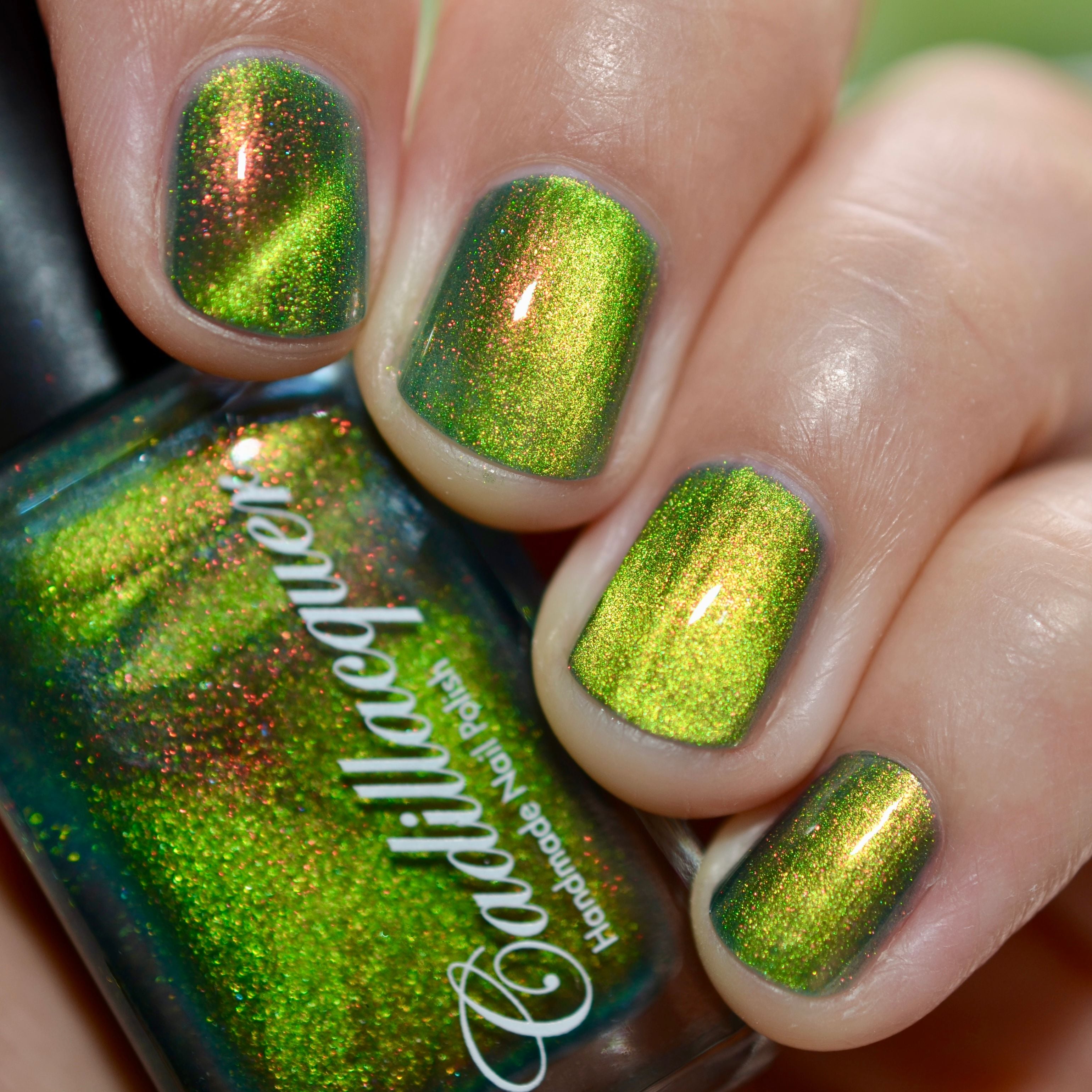 Magnetic multichrome shimmer Cadillacquer nail polish in I Found A Place, shown on four short natural nails with a matching bottle, displaying a deep olive-green carrier base with a bright lime-yellow magnetic band stripe and vivid red-to-orange aurora shimmer flash, light skin tone, bright daylight lighting, swatched by @caitlinswatches