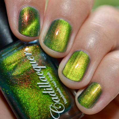 Magnetic multichrome shimmer Cadillacquer nail polish in I Found A Place, shown on four short natural nails with a matching bottle, displaying a deep olive-green carrier base with a bright lime-yellow magnetic band stripe and vivid red-to-orange aurora shimmer flash, light skin tone, bright daylight lighting, swatched by @caitlinswatches