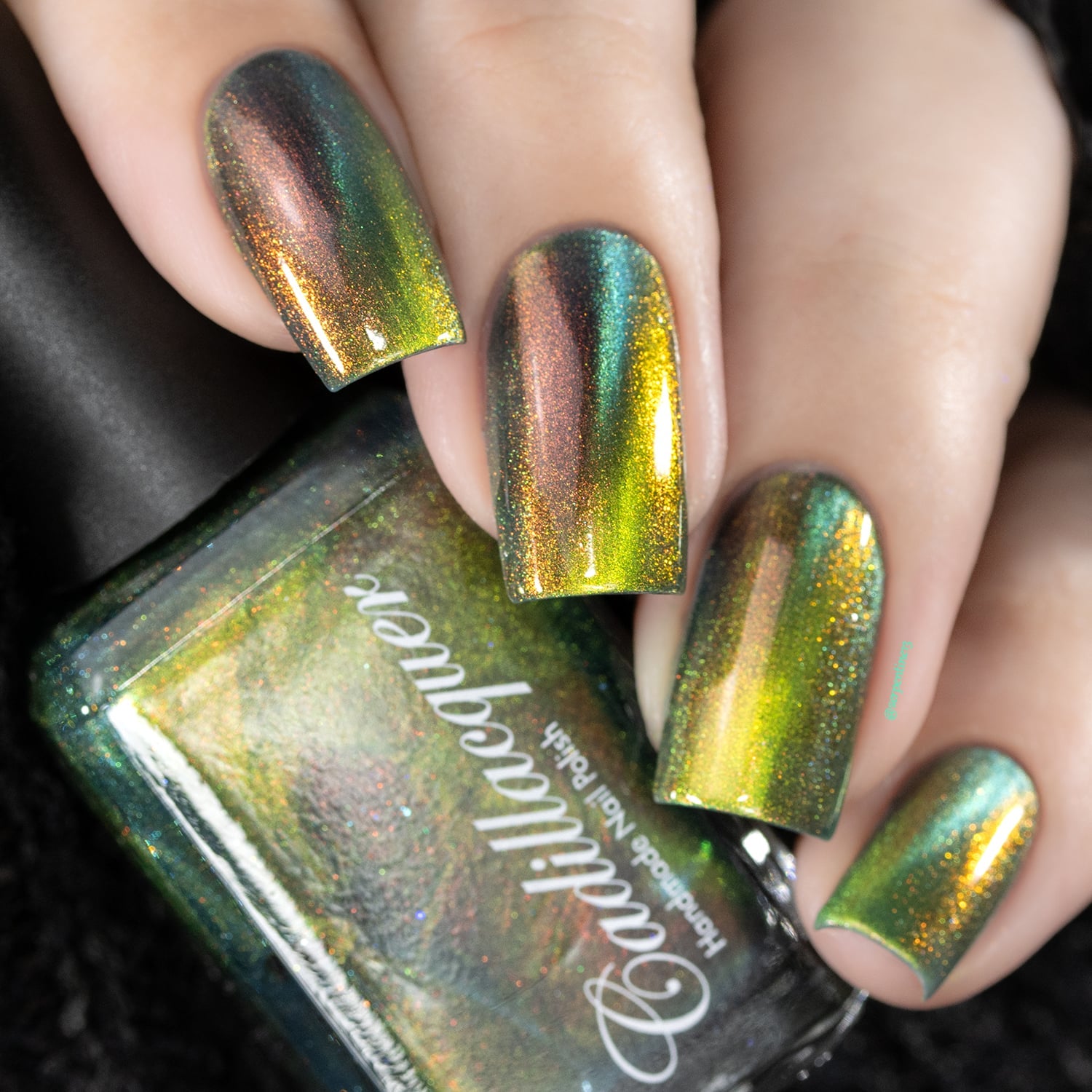 Multichrome holographic magnetic Cadillacquer nail polish in I Found A Place, shown on four square nails with a deep olive-teal carrier base shifting through copper-red and amber-gold, with a bright amber-gold magnetic band stripe and fine holographic red-to-orange aurora shimmer throughout, held alongside the bottle, light skin tone, studio lighting, swatched by @serpentine13