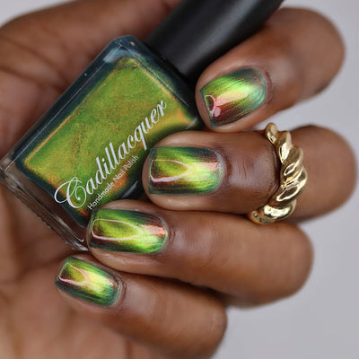 Magnetic multichrome Cadillacquer nail polish in I Found A Place, swatched on five short square nails with a bold lime-chartreuse magnetic cat-eye band over a deep forest green field, flashing burnt orange-red aurora shimmer at angle, bottle shows deep teal carrier base with scattered copper and olive shimmer, deep skin tone, gold twisted ring visible, studio lighting, swatched by @lacquer_is_life