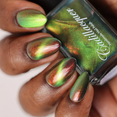Magnetic multichrome shimmer Cadillacquer nail polish in I Found A Place, swatched on almond-shaped nails showing a bright lime-yellow magnetic cat-eye band over a deep olive-green base with vivid red-orange aurora shimmer flash, held alongside the matching bottle, rich skin tone, studio lighting, swatched by @doseoflolade