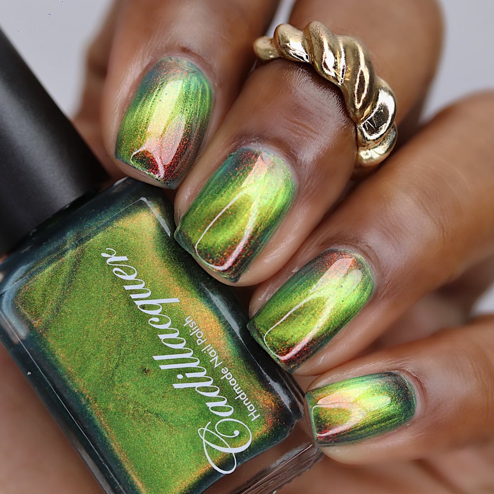 Magnetic multichrome shimmer Cadillacquer nail polish in I Found A Place, shown on five short square nails with a deep skin tone alongside the polish bottle, the nails display a bright lime-chartreuse magnetic cat-eye stripe over a deep forest green field, shifting through burnt red-orange aurora shimmer at low angles, photographed in studio lighting with a gold twisted ring accent, swatched by @lacquer_is_life