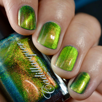 Magnetic multichrome shimmer Cadillacquer nail polish in I Found A Place, shown on four short natural nails with a bottle in hand, displaying bright lime-green magnetic band over a teal-green field base with red-to-orange aurora shimmer scatter, on light-medium skin, under studio lighting, swatched by @caitlinswatches