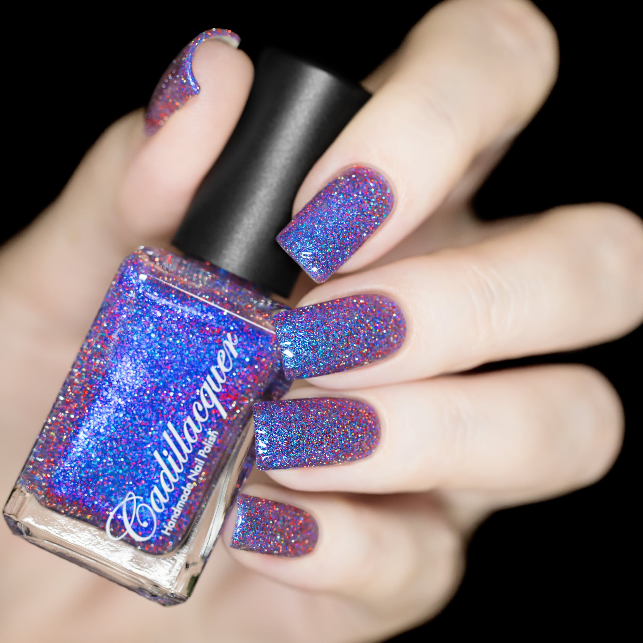 Holographic shimmer and glitter Cadillacquer nail polish in I'll Be Right Back, shown as bottle-in-hand with five square nails swatched, polish is a clear base densely packed with blue micro flakes, blue shimmer, and red and silver reflective holographic glitter producing a vibrant blue-violet effect on the nail, light skin tone, studio lighting, swatched by @rafinails