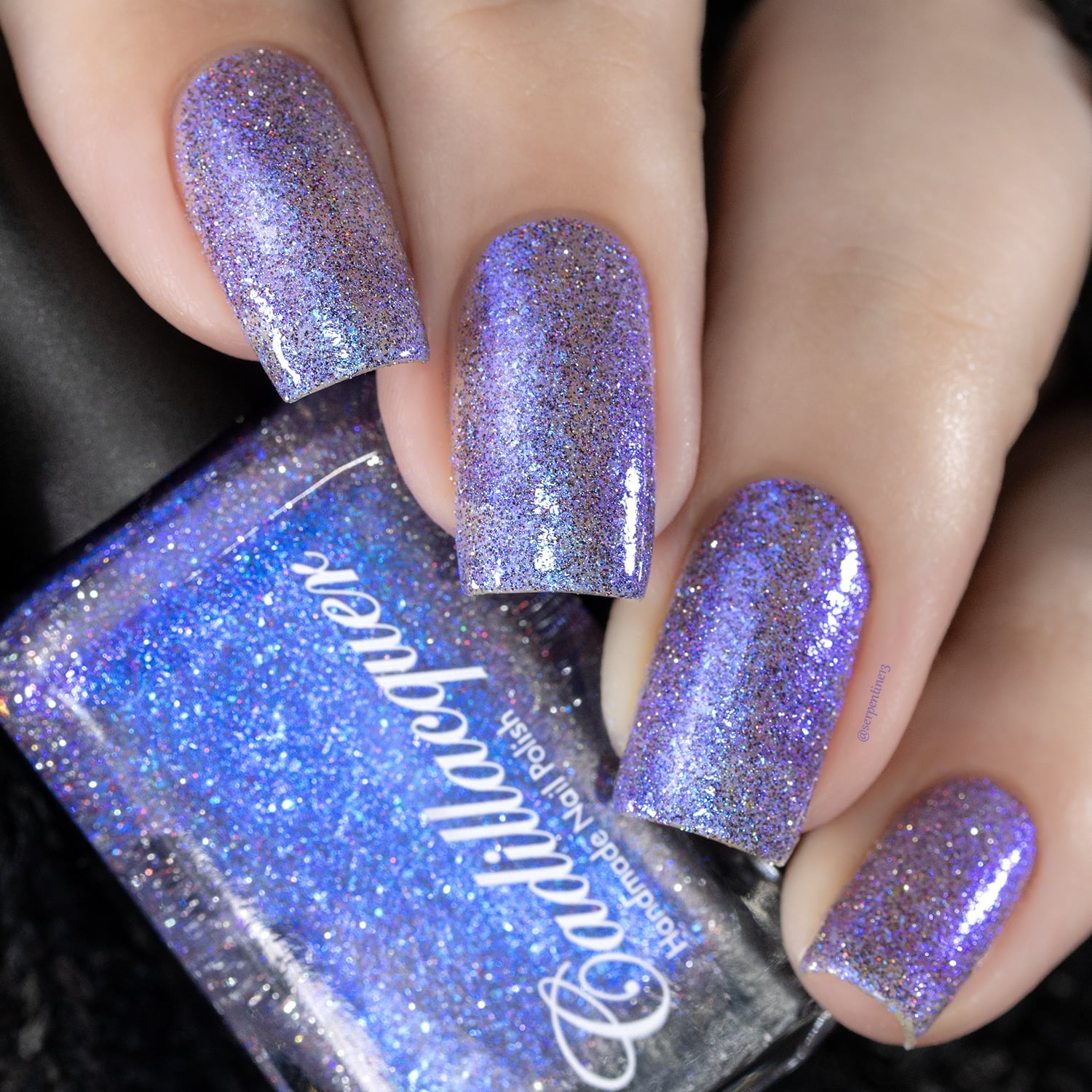 Holographic shimmer and micro-flake Cadillacquer nail polish in I'll Be Right Back, shown swatched on five square nails alongside the bottle, lavender-purple base packed with blue micro flakes, blue shimmer flash, and charcoal and red reflective holographic micro glitter, light skin tone, studio lighting, swatched by @serpentine13