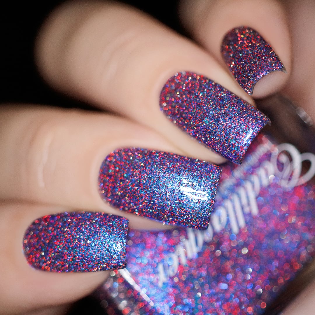 Glitter and shimmer Cadillacquer nail polish in I'll Be Right Back, shown on five squoval nails in a close-up studio shot, dense blue-violet clear base packed with red holographic micro glitter, blue micro flakes, and a bright cornflower-blue shimmer flash, on light-medium skin tone, studio lighting, swatched by @yyulia_m
