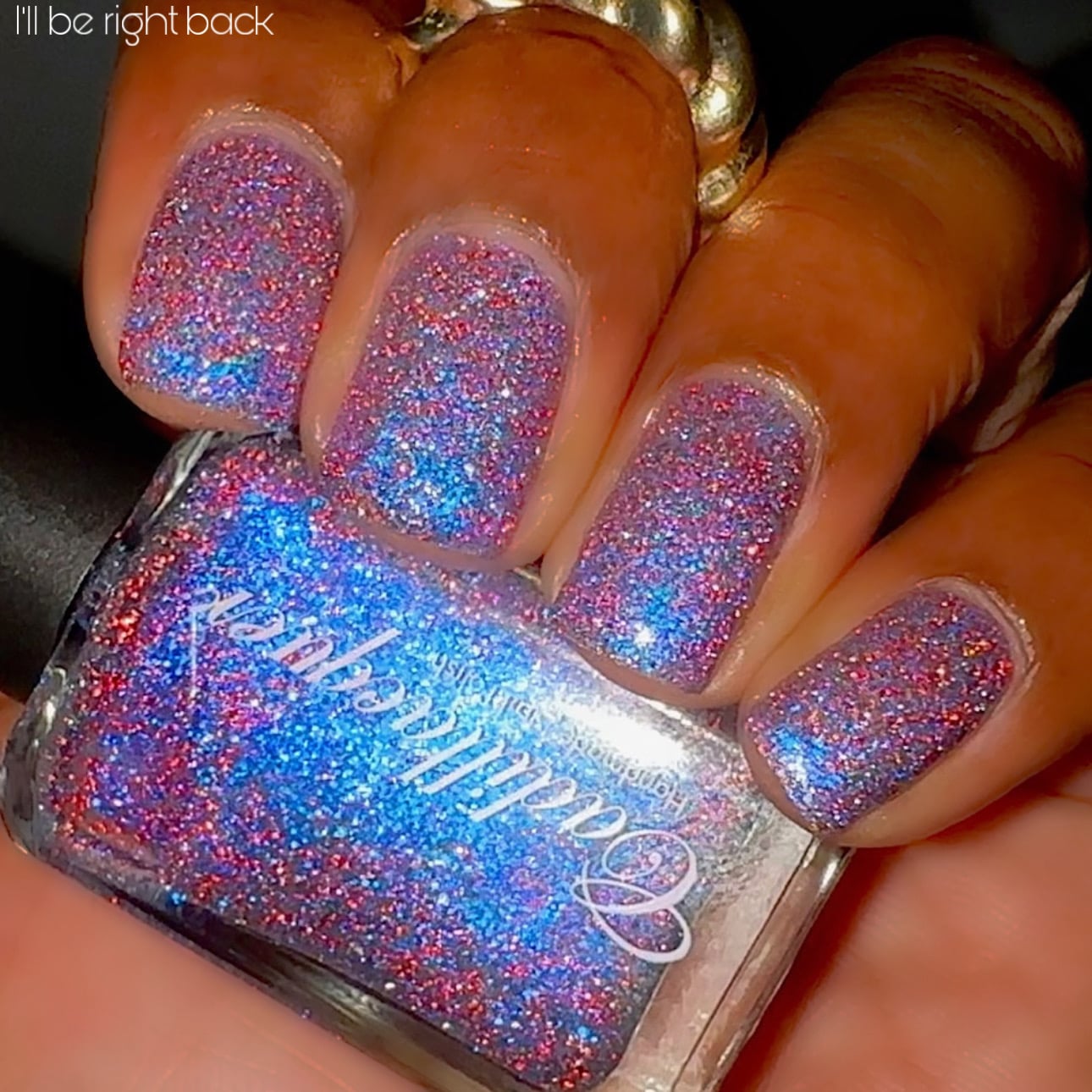 Shimmer, glitter and micro-flake Cadillacquer nail polish in I'll Be Right Back, shown as swatches on eight squoval nails held around a clear polish bottle, packed with electric blue micro flakes, hot pink-red and silver reflective glitter, and blue shimmer over a sheer base, medium skin tone, direct flash lighting, swatched by @lacquer_is_life