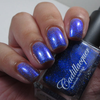 Shimmer, micro-flake and reflective glitter Cadillacquer nail polish in I'll Be Right Back, shown swatched on eight short natural nails held alongside the deep navy bottle, light-medium skin tone, indoor warm lighting, swatched by @_always_polished_