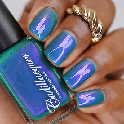 Multichrome shimmer Cadillacquer nail polish in It's All For You, shown in bottle held in hand alongside swatched nails, shifting between teal green base and violet-purple shimmer flash at angular highlights, worn on deep skin tone with squoval nails and gold twisted ring, studio lighting, swatched by @lacquer_is_life