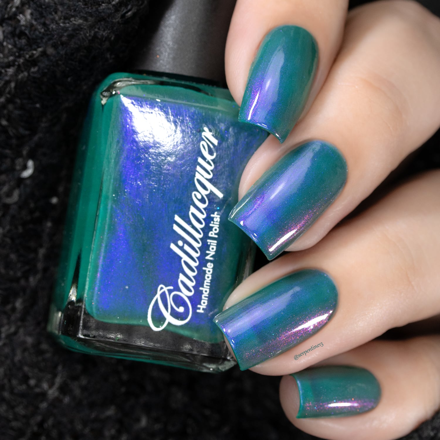 Multichrome shimmer Cadillacquer nail polish in It's All For You, shown in bottle held in hand with four square-shaped swatched nails, shifting from teal-green base through violet-purple to magenta-pink depending on angle, light skin tone, studio lighting, swatched by @serpentine13
