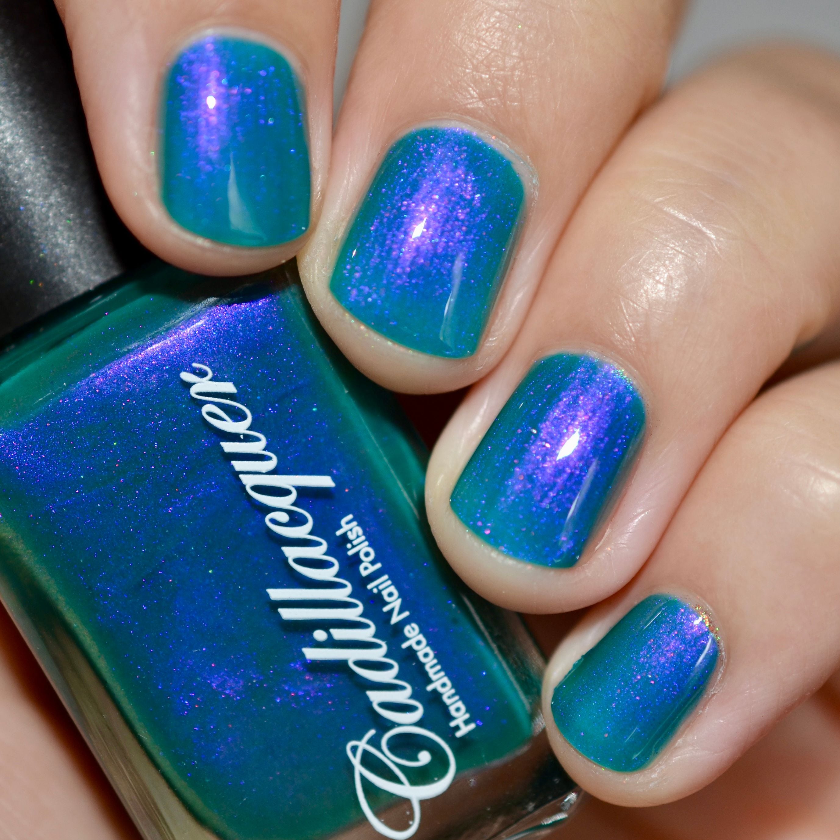 Multichrome shimmer crelly Cadillacquer nail polish in It's All For You, shown in bottle held alongside four swatched nails on light skin, shifting from teal green base to violet-purple and blue-violet shimmer flash, studio lighting, swatched by @caitlinswatches