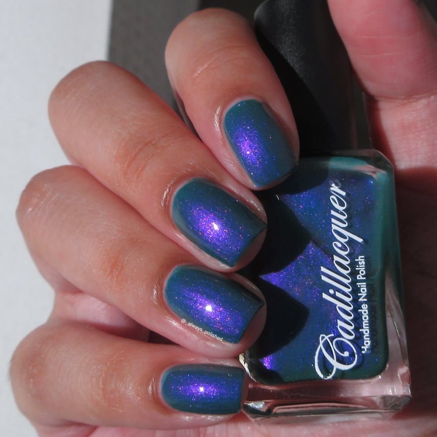 Shimmer multichrome Cadillacquer nail polish in It's All For You, shown on eight squoval nails with a teal green base packed with vivid violet-purple shimmer that flashes blue and hot pink at different angles, held alongside the matching bottle, light skin tone, studio lighting, swatched by @_always_polished_