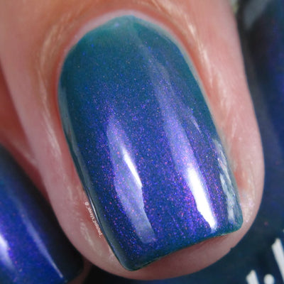 Multichrome shimmer Cadillacquer nail polish in It's All For You, single nail swatch showing teal green base shifting to deep indigo-blue and violet-purple with magenta shimmer sparks, light skin tone, studio lighting, swatched by @_always_polished_
