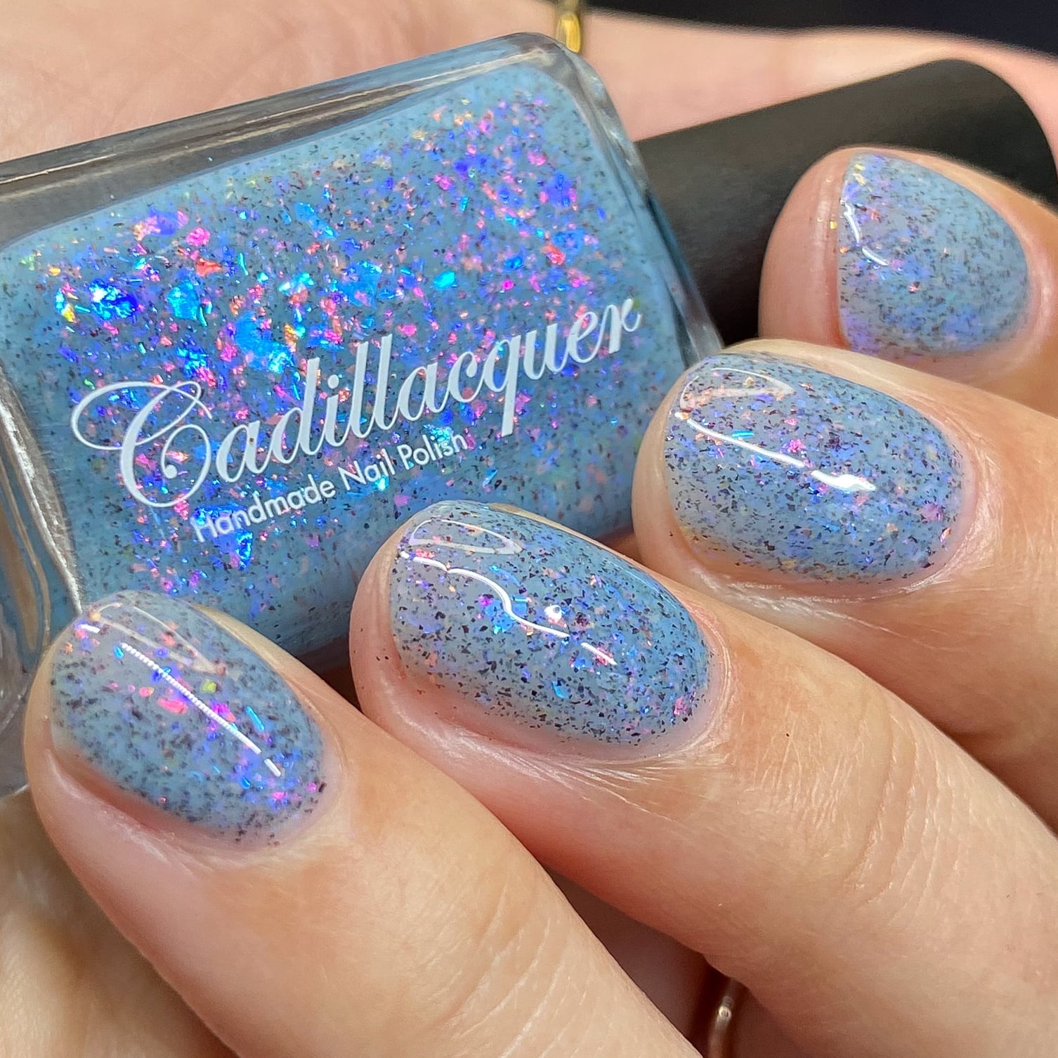 Cadillacquer Just Breathe pastel blue iridescent crelly nail polish, bottle held with four-nail swatch, light skin, bright daylight lighting