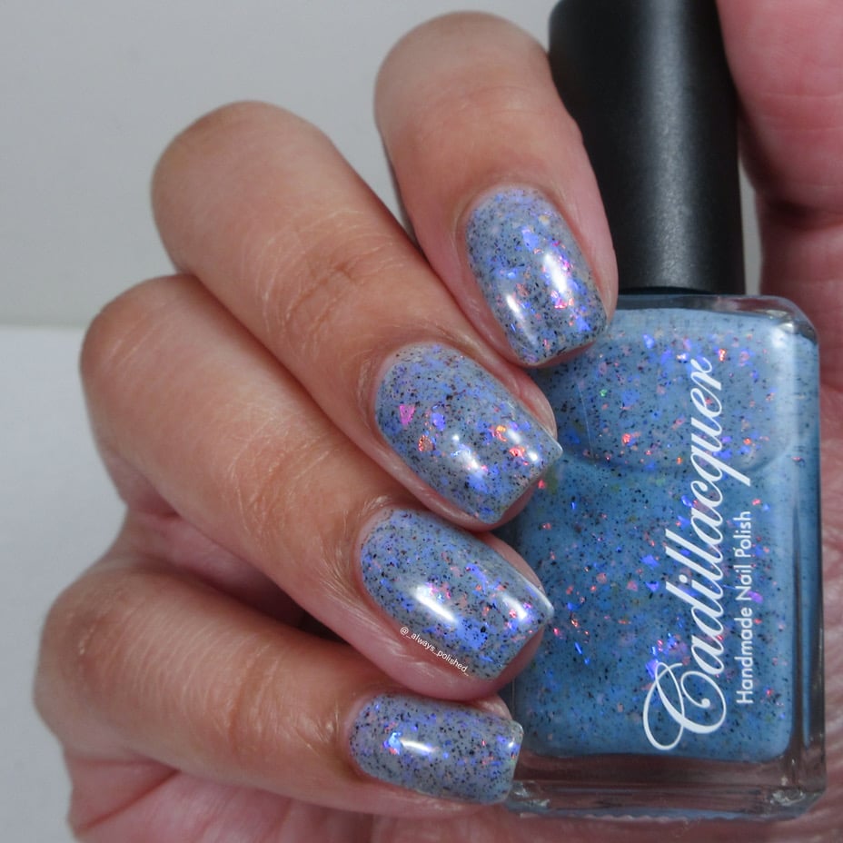 Cadillacquer Just Breathe pastel blue iridescent crelly nail polish, bottle held with four-nail swatch, light skin, bright daylight lighting