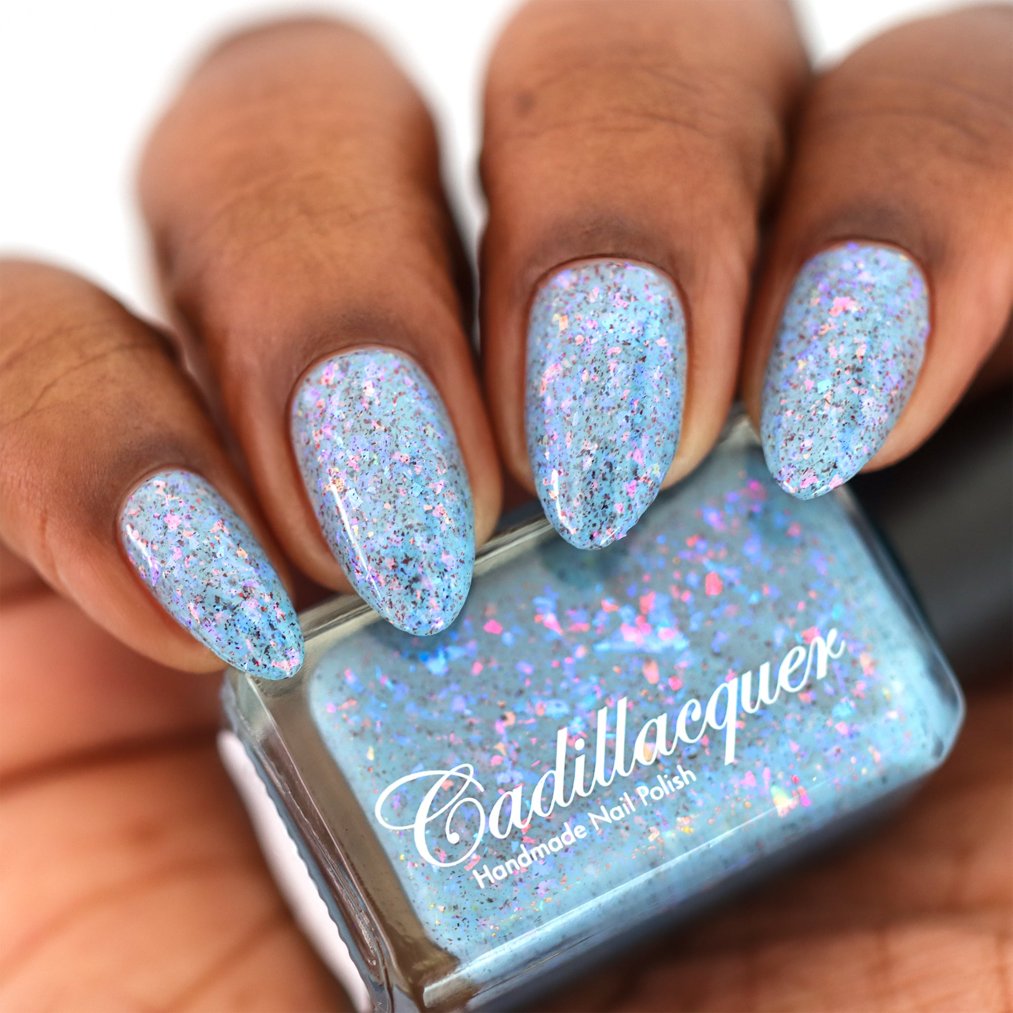 Cadillacquer Just Breathe pastel blue iridescent crelly nail polish, bottle held with four-nail swatch, deep skin, studio lighting