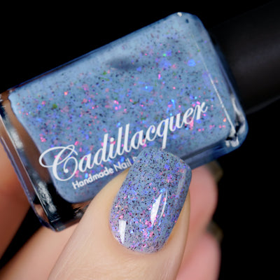 Cadillacquer Just Breathe pastel blue iridescent crelly nail polish, bottle held with one-nail swatch, light skin, studio lighting