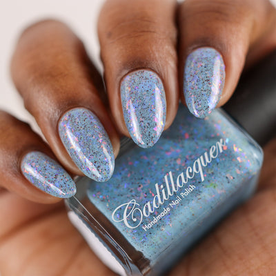 Cadillacquer Just Breathe pastel blue iridescent crelly nail polish, bottle held with four-nail swatch, deep skin, studio lighting