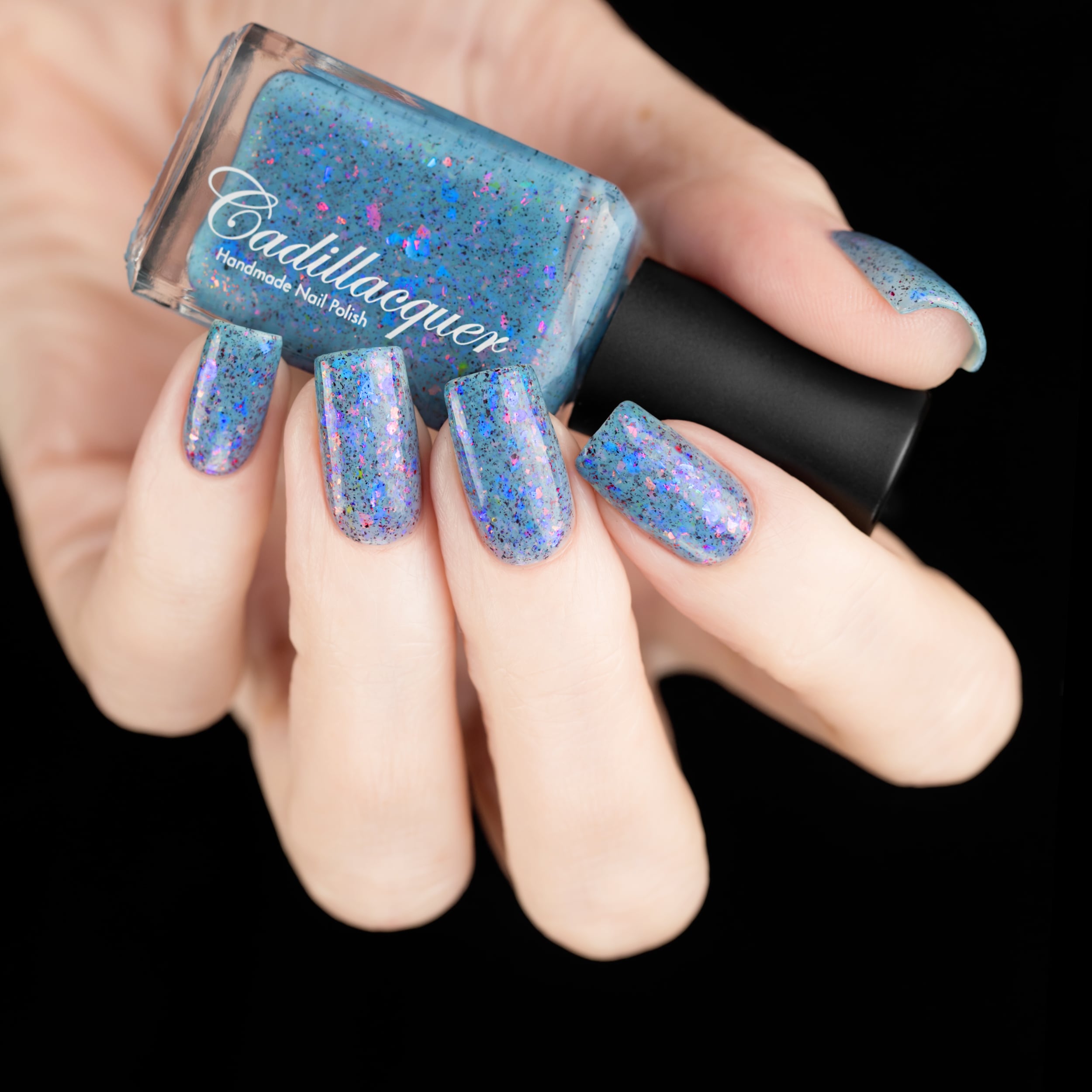 Cadillacquer Just Breathe pastel blue iridescent crelly nail polish, bottle held with five-nail swatch, light skin, studio lighting