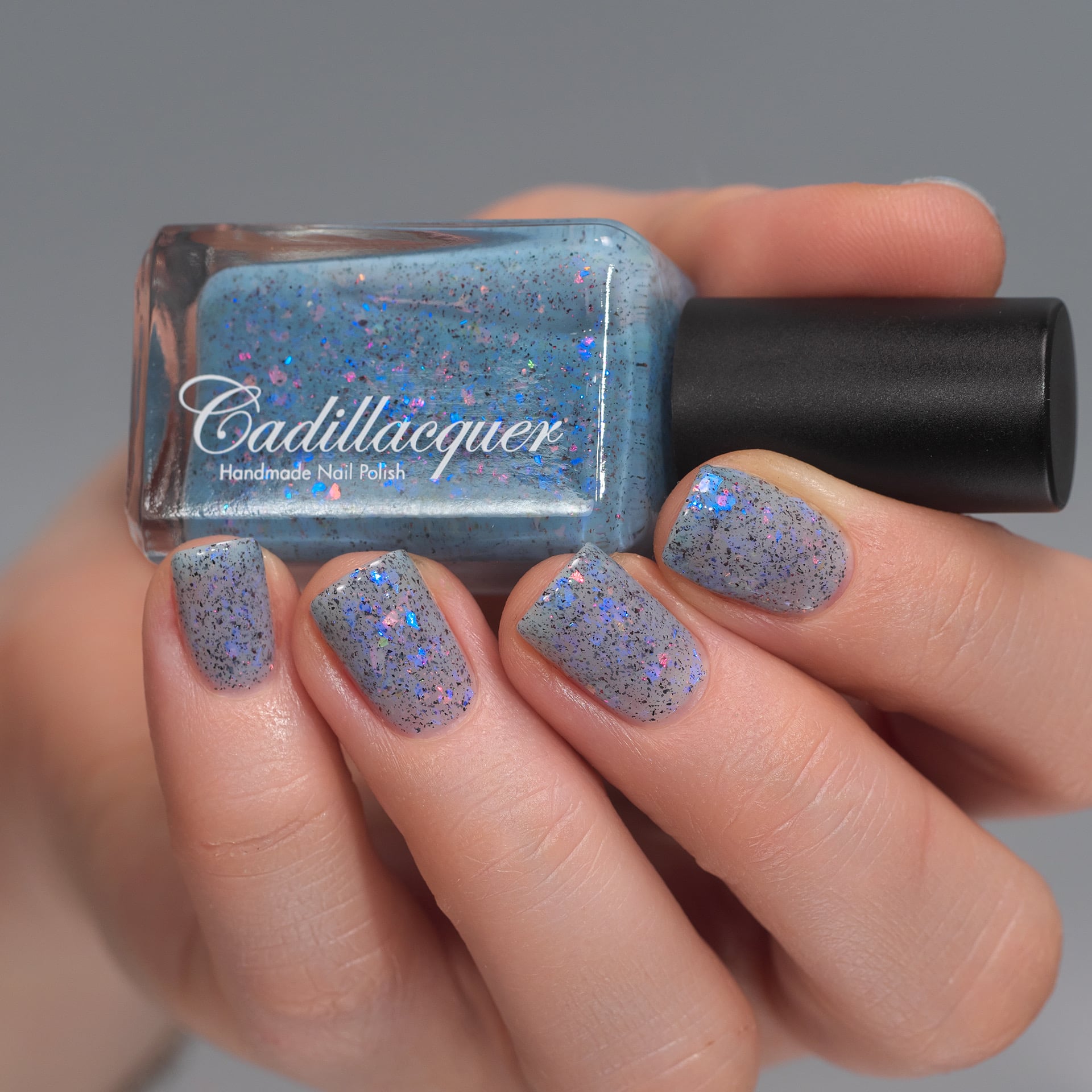 Cadillacquer Just Breathe pastel blue iridescent crelly nail polish, bottle held with four-nail swatch, light skin, studio lighting