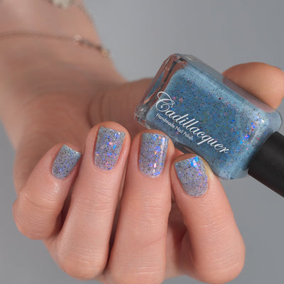 Cadillacquer Just Breathe pastel blue iridescent crelly nail polish, bottle held with four-nail swatch, light skin, studio lighting