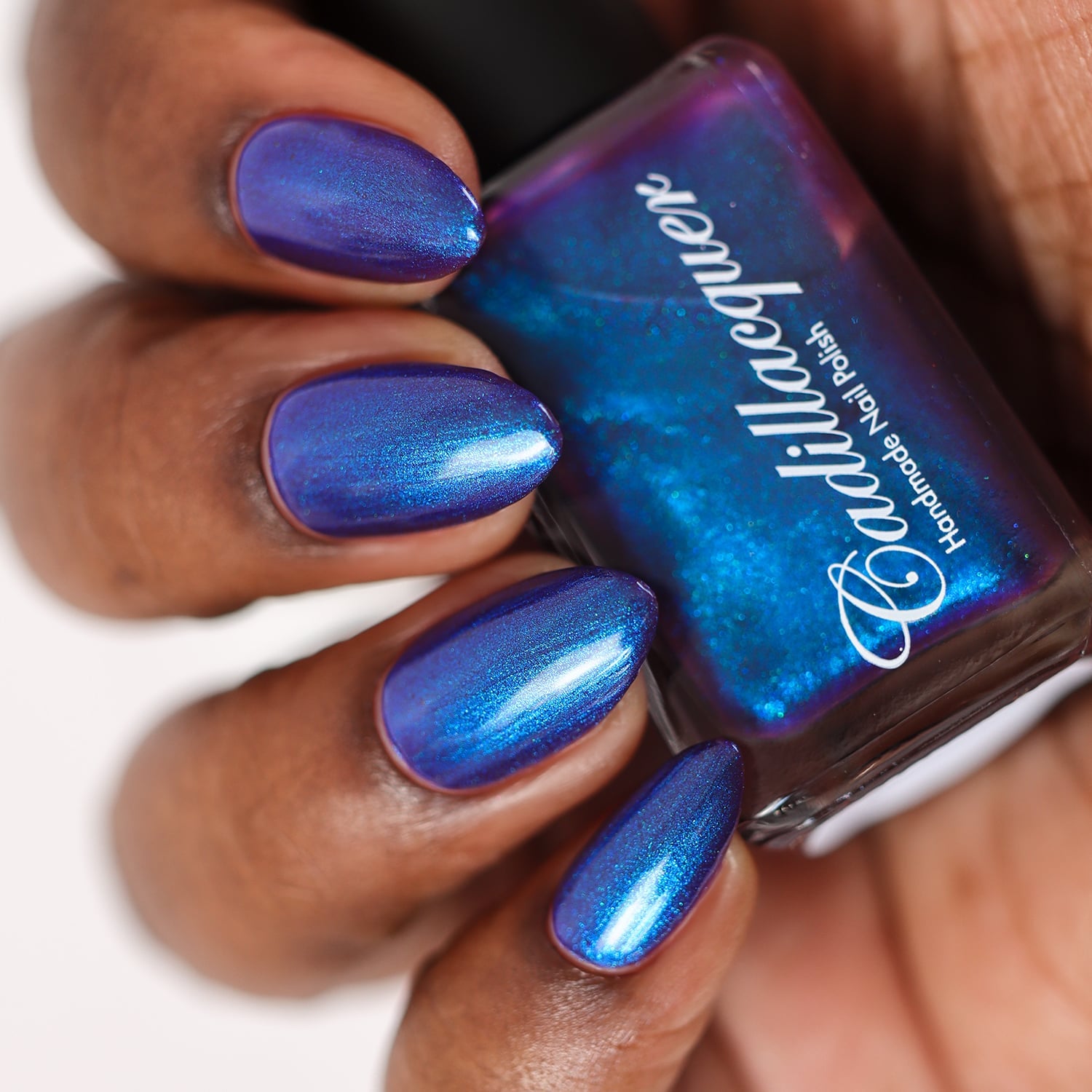 Multichrome shimmer Cadillacquer nail polish in Keep Doubting, shown as bottle-in-hand swatch with four almond-shaped nails on deep skin tone, base shifts from deep violet-indigo to electric cobalt blue and teal depending on angle, bottle face dominated by bright cerulean shimmer, studio lighting, swatched by @doseoflolade