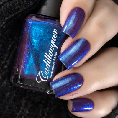Shimmer multichrome Cadillacquer nail polish in Keep Doubting, shown in a bottle-in-hand shot with four square nails swatched, displaying a deep mulberry-purple base shifting to bright electric blue and teal shimmer flash, light skin tone, studio lighting, swatched by @serpentine13