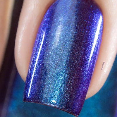 Holographic shimmer Cadillacquer nail polish in Keep Doubting, extreme macro close-up of a single square nail showing deep violet-purple base densely packed with electric blue and cyan holographic shimmer particles that form a luminous central band, light-medium skin tone visible at edges, studio lighting, swatched by @serpentine13