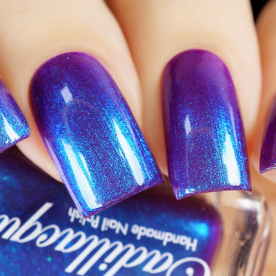 Shimmer Cadillacquer nail polish swatch in Keep Doubting, showing deep violet-mulberry base densely packed with vivid cobalt-blue and cyan shimmer that shifts across the nail surface, worn on five oval nails on light skin tone, shot under studio lighting with a Cadillacquer bottle in the foreground, swatched by @yyulia_m