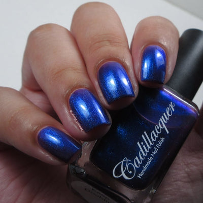 Shimmer and reflective Cadillacquer nail polish in Keep Doubting, shown on eight squoval nails with deep violet-indigo base packed with vivid royal blue shimmer, alongside the dark navy bottle, on light-medium skin tone, indoor lighting, swatched by @_always_polished_
