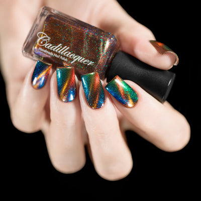 Magnetic holographic multichrome Cadillacquer nail polish in Once You See It, shown in bottle held in hand with five swatched square nails displaying dramatic diagonal copper-orange magnetic band over deep teal-blue field with vivid green and blue aurora shimmer, light skin tone, studio lighting, swatched by @rafinails