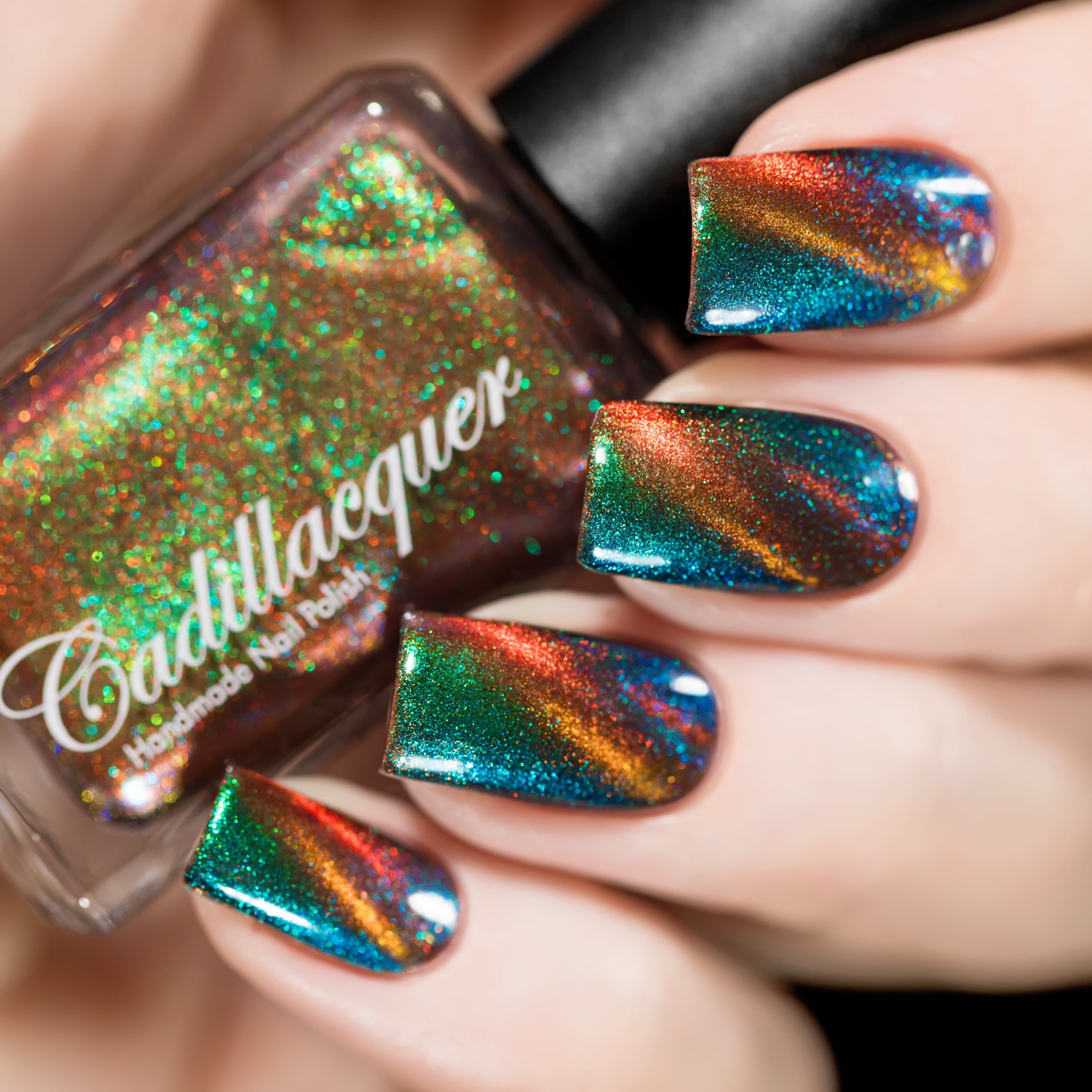 Holographic magnetic multichrome Cadillacquer nail polish in Once You See It, shown in bottle held against four swatched nails displaying vivid green-to-blue aurora shimmer with an orange magnetic band stripe across a deep teal field, light skin tone, studio lighting, swatched by @rafinails
