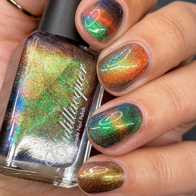 Magnetic multichrome holographic Cadillacquer nail polish in Once You See It, shown on five short natural nails with a swirl magnetic pattern and the matching bottle, the field reads very dark reddish-brown while a vivid copper-orange magnetic band arcs across each nail, with green-to-blue aurora shimmer flashing throughout, light-medium skin tone, studio lighting, swatched by @heeymercedes