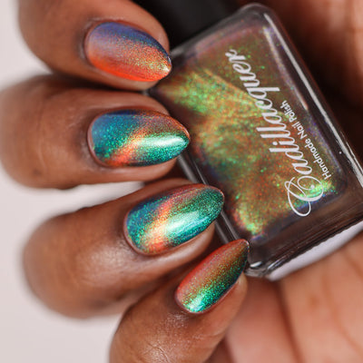 Multichrome magnetic shimmer Cadillacquer nail polish in Once You See It, five almond-shaped nails on rich skin holding a dark green bottle, nails shifting from deep teal-green field to vivid orange-red magnetic band with emerald and blue aurora shimmer flash throughout, studio lighting, swatched by @doseoflolade