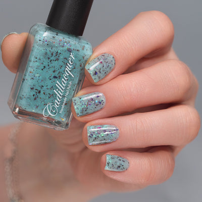 Cadillacquer Pastel Thoughts pastel teal purple chameleon iridescent crelly nail polish, bottle held with four-nail swatch, light skin, studio lighting