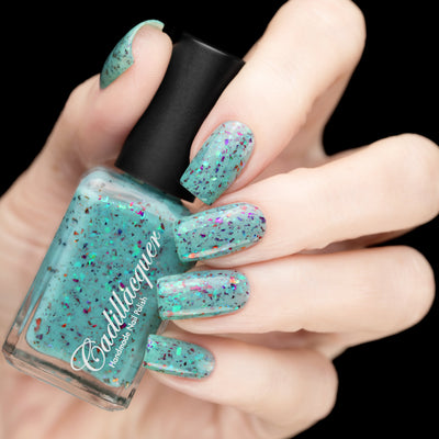 Cadillacquer Pastel Thoughts pastel teal purple chameleon iridescent crelly nail polish, bottle held with five-nail swatch, light skin, studio lighting
