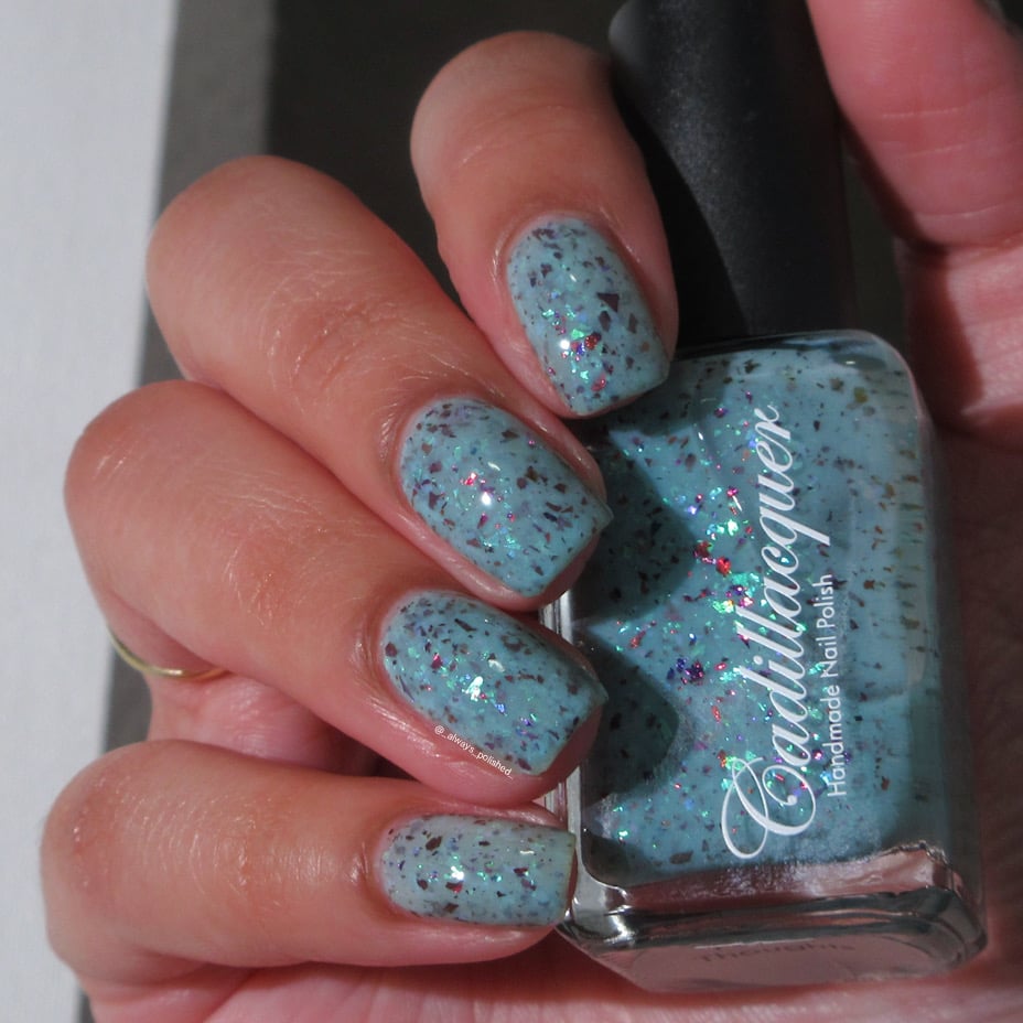 Cadillacquer Pastel Thoughts pastel teal purple chameleon iridescent crelly nail polish, bottle held with four-nail swatch, light-medium skin, indoor warm lighting