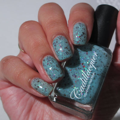 Cadillacquer Pastel Thoughts pastel teal purple chameleon iridescent crelly nail polish, bottle held with four-nail swatch, light skin, bright daylight lighting