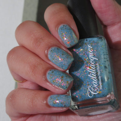 Cadillacquer Slow Mornings light blue gold chameleon iridescent crelly nail polish, bottle held with four-nail swatch, light skin, bright daylight lighting