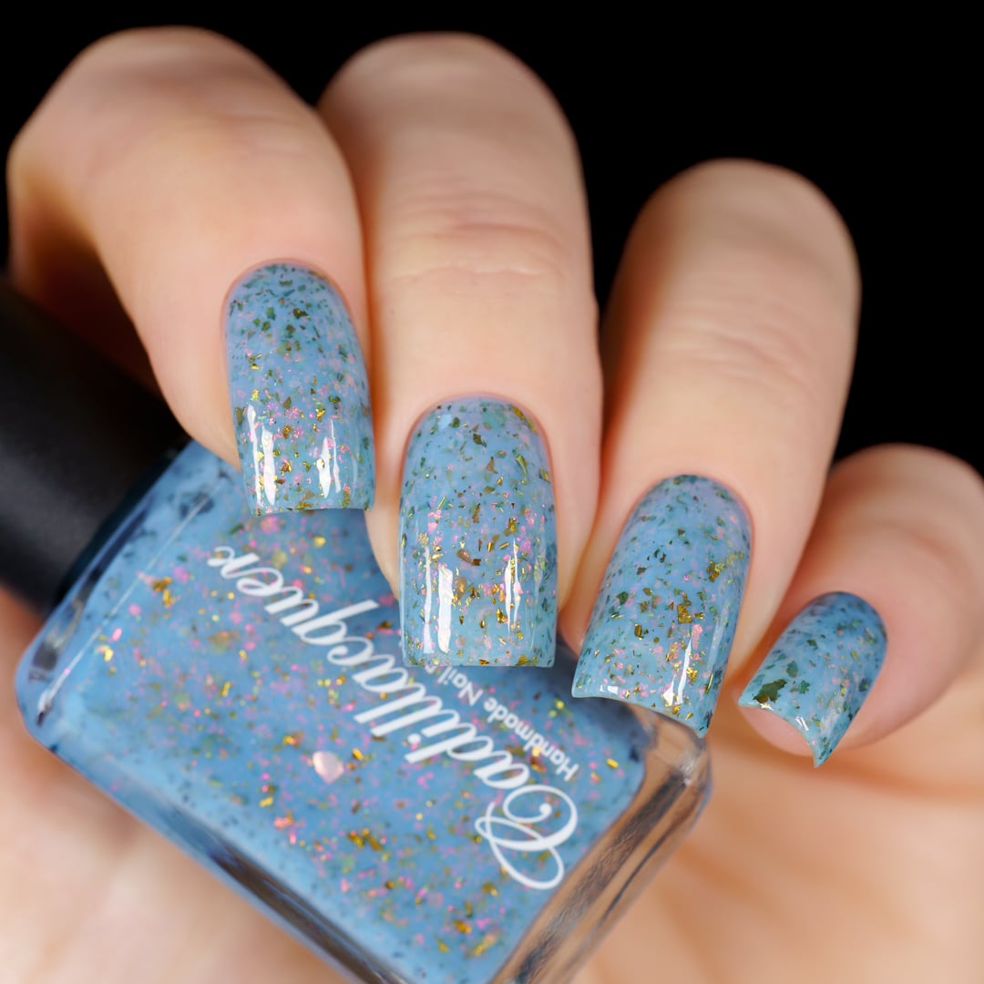 Cadillacquer Slow Mornings light blue gold chameleon iridescent crelly nail polish, bottle held with four-nail swatch, light skin, studio lighting