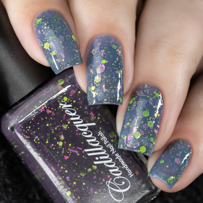 Thermal glitter-and-flake Cadillacquer nail polish in Strange Happenings, shown on four square nails at the warm dusty blue-grey state alongside a bottle in the dark blackened eggplant cold state, packed with matte neon yellow-green glitter in dot and hexagon shapes and large iridescent flakes shifting from hot pink to golden-orange and violet, light skin tone, studio lighting, swatched by @serpentine13