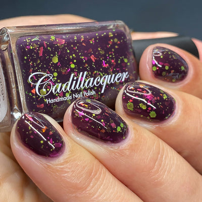 Thermal glitter and flake Cadillacquer nail polish in Strange Happenings, shown in a bottle-in-hand swatch with five short natural nails on light skin, the blackened eggplant purple base is loaded with neon yellow-green matte glitter in large hex and small dot sizes plus hot pink and orange iridescent flakes, photographed under studio lighting, swatched by @heeymercedes