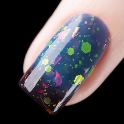 Thermal glitter and iridescent flake Cadillacquer nail polish in Strange Happenings, macro swatch on a single square nail showing deep blackened eggplant cold state transitioning to dusty blue warm state, packed with matte neon green hexagonal glitter in multiple sizes and large pink-to-amber iridescent flakes, light skin tone, studio lighting, swatched by @rafinails