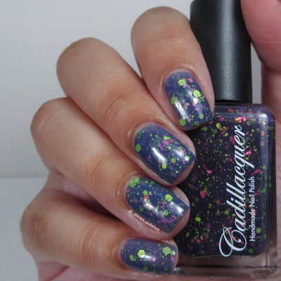 Thermal glitter-and-flake Cadillacquer nail polish in Strange Happenings, shown swatched on four short natural nails held alongside the bottle, nails display the warm dusty slate-blue state loaded with matte neon green hex and dot glitter and hot-pink iridescent flakes, while the bottle shows the dark blackened eggplant cold state, light skin tone, studio lighting, swatched by @_always_polished_