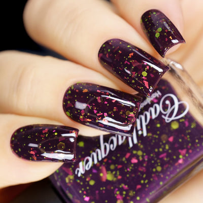Thermal glitter-and-flake Cadillacquer nail polish in Strange Happenings, shown swatched on four medium-length square nails in the cold state, a deep blackened eggplant base densely scattered with matte neon chartreuse green glitter in mixed sizes and hot pink to orange iridescent flakes, a matching bottle is partially visible, on light skin, in studio lighting, swatched by @yyulia_m